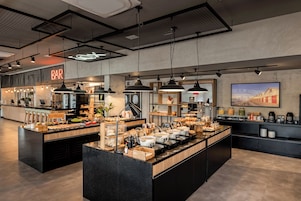 A modern bar area with a neon sign, pendant lighting, and a variety of food and drink options.