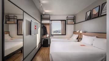 A hotel room with two beds, a small desk, a mirror, a TV, and a window with a city view.