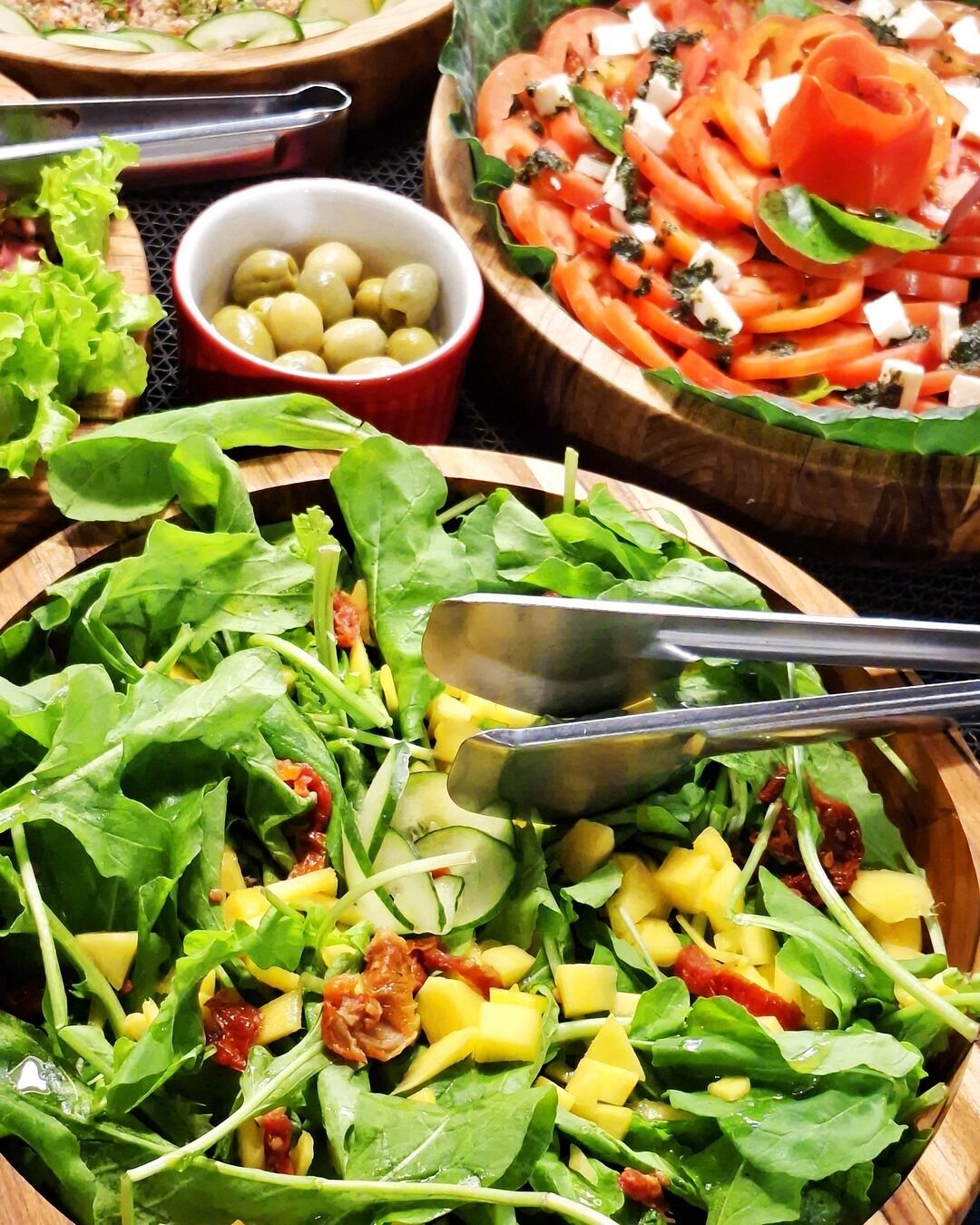 Diversas saladas e uma tigela de azeitonas sobre uma mesa de madeira.