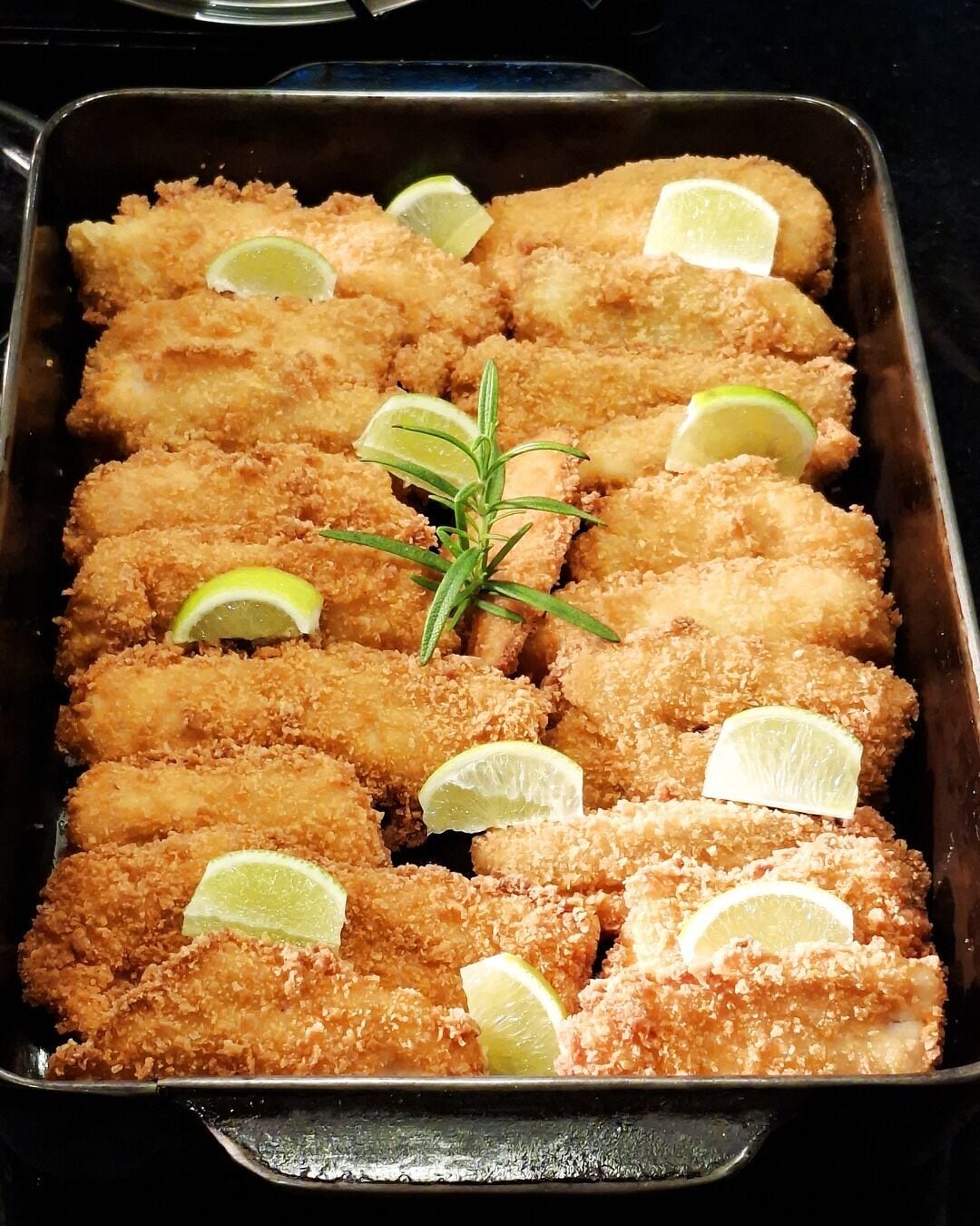 A tray of breaded and fried food items garnished with lime slices and a sprig of rosemary.