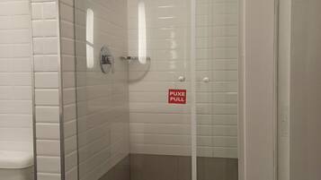 Un box de ducha con paredes de azulejos blancos, un secamanos visible y un cartel que dice 'PUXE PULL'.