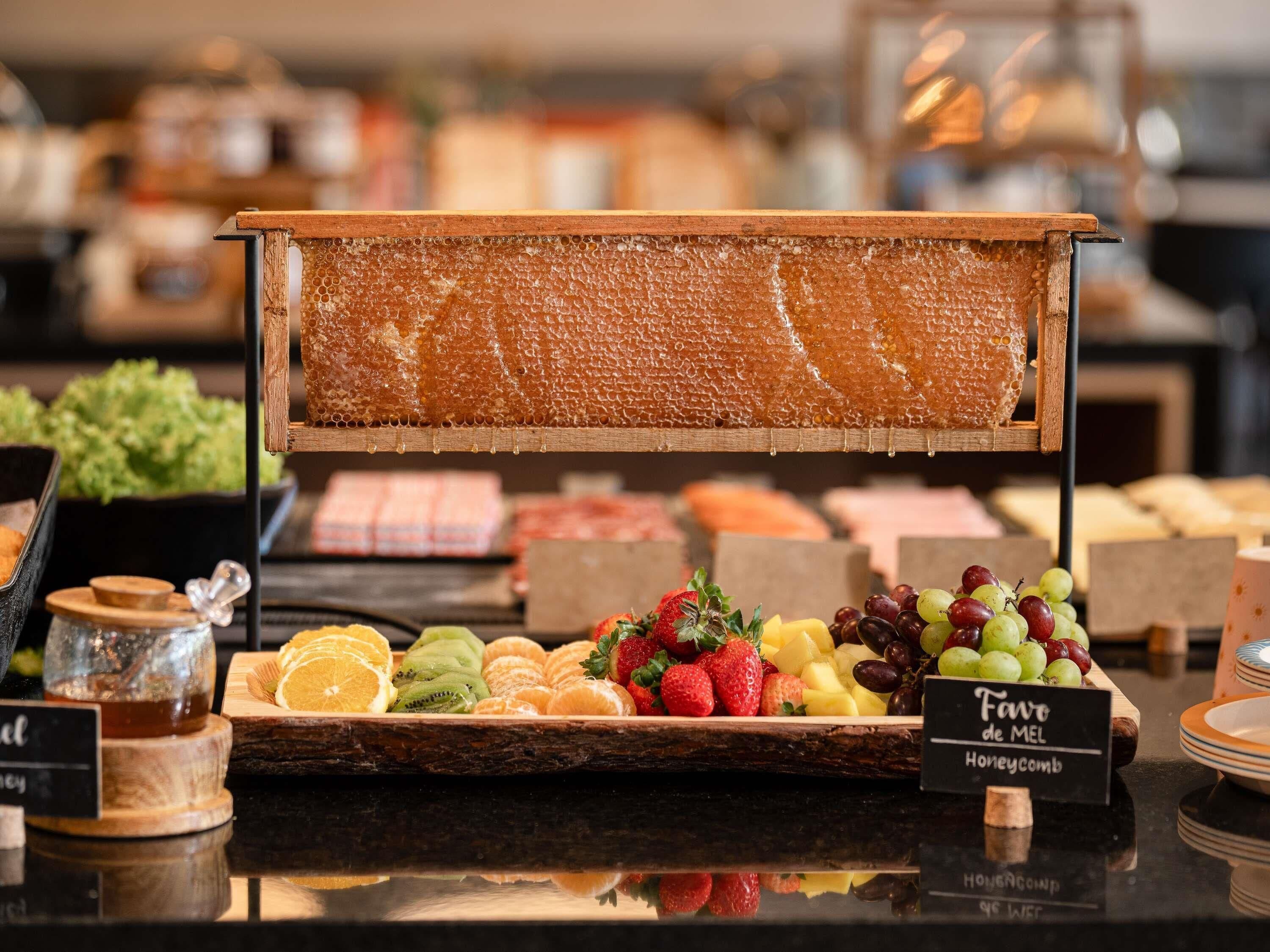 A buffet table with a honeycomb display, a variety of fruits, and a sign indicating 'Fave de MEL Honeycomb'.