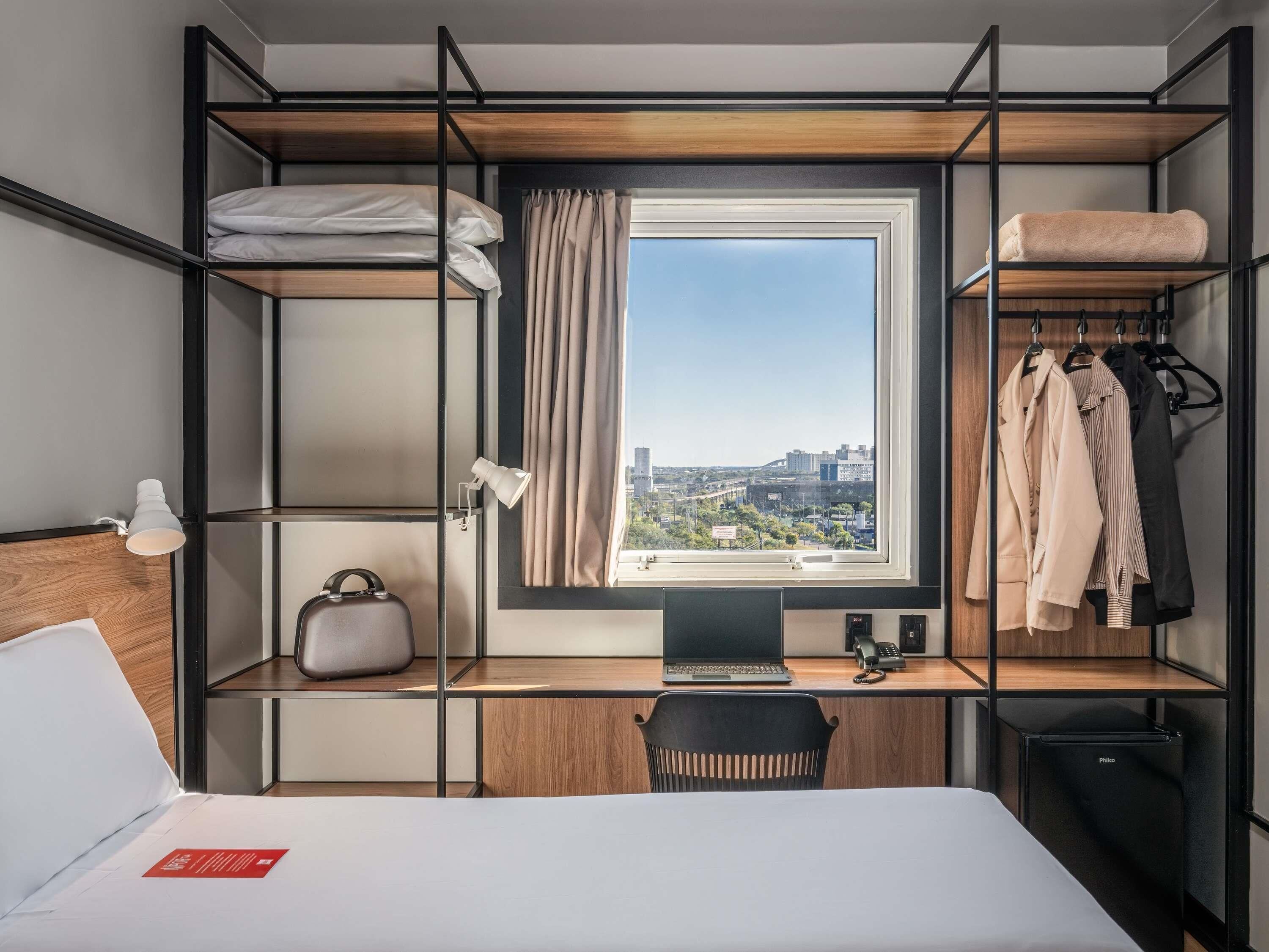 Una habitación de hotel pequeña con cama, escritorio y armario.