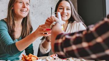 Two people toasting with drinks at a table with food.