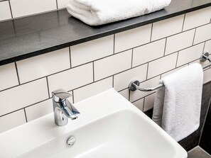 Un baño con lavamanos blanco, encimera negra y un perchero.