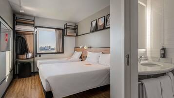 A hotel room with a bed, a bedside table, a window, a bathroom with a sink, and a towel rack.