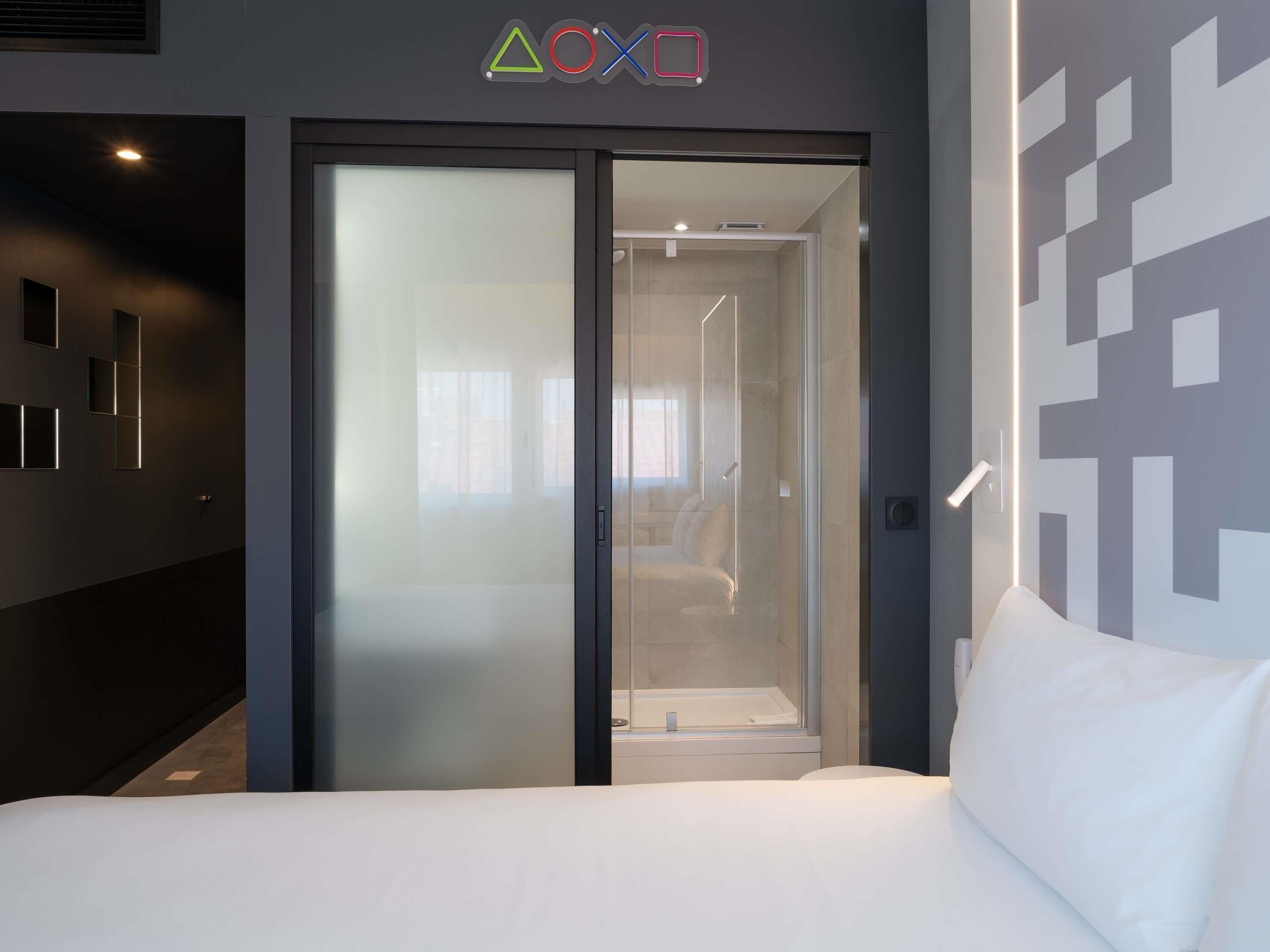 Una habitación de hotel con una cama, una puerta corredera que da a un baño y una pared con diseños geométricos.