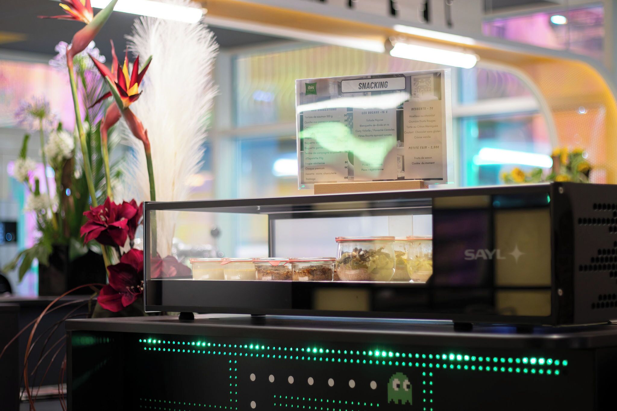 A vending machine with a menu display, surrounded by decorative plants.