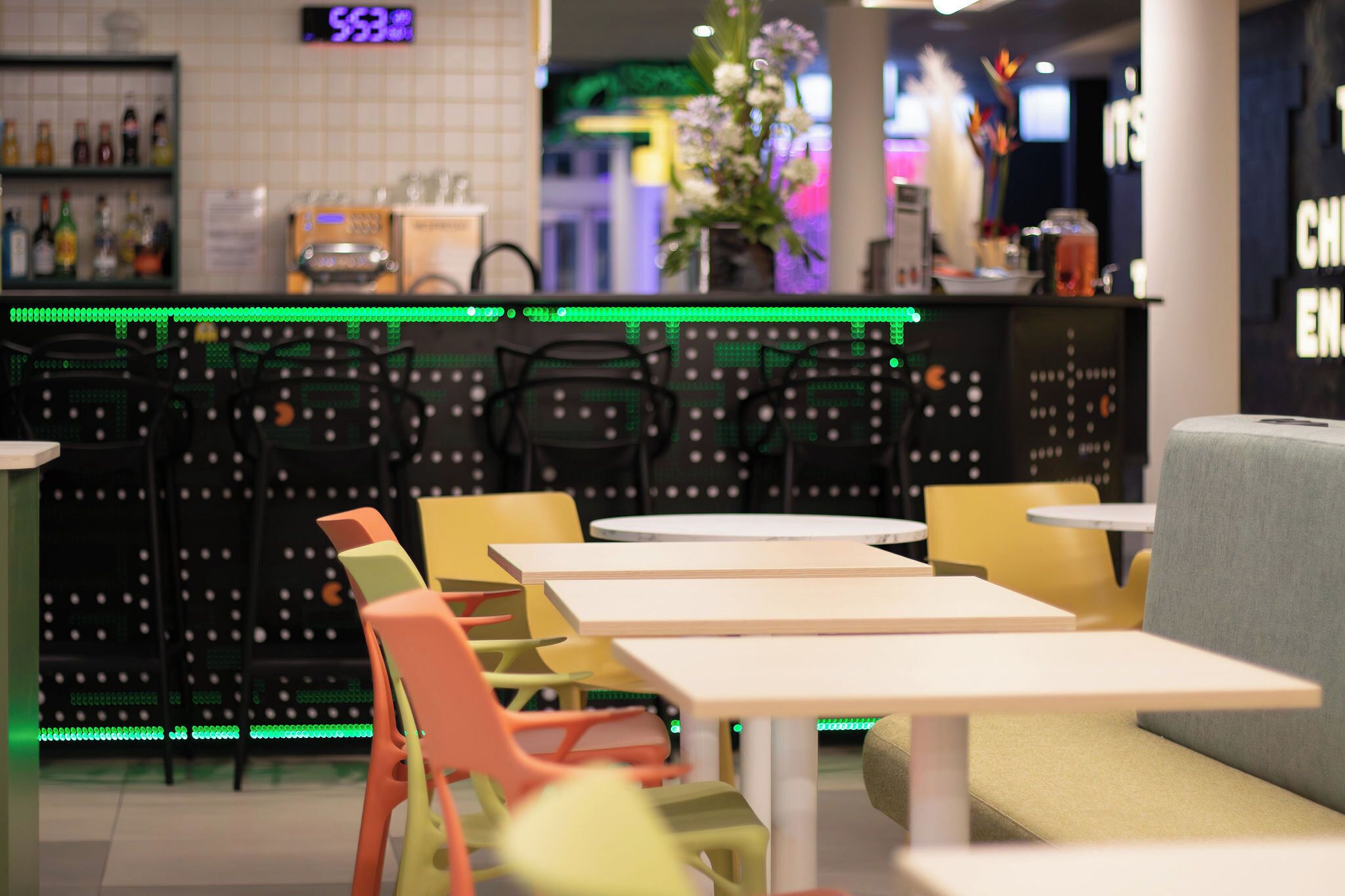 Interior moderno de una cafetería con barra, diversas opciones de asientos, incluyendo sillas y mesas, y una planta decorativa.
