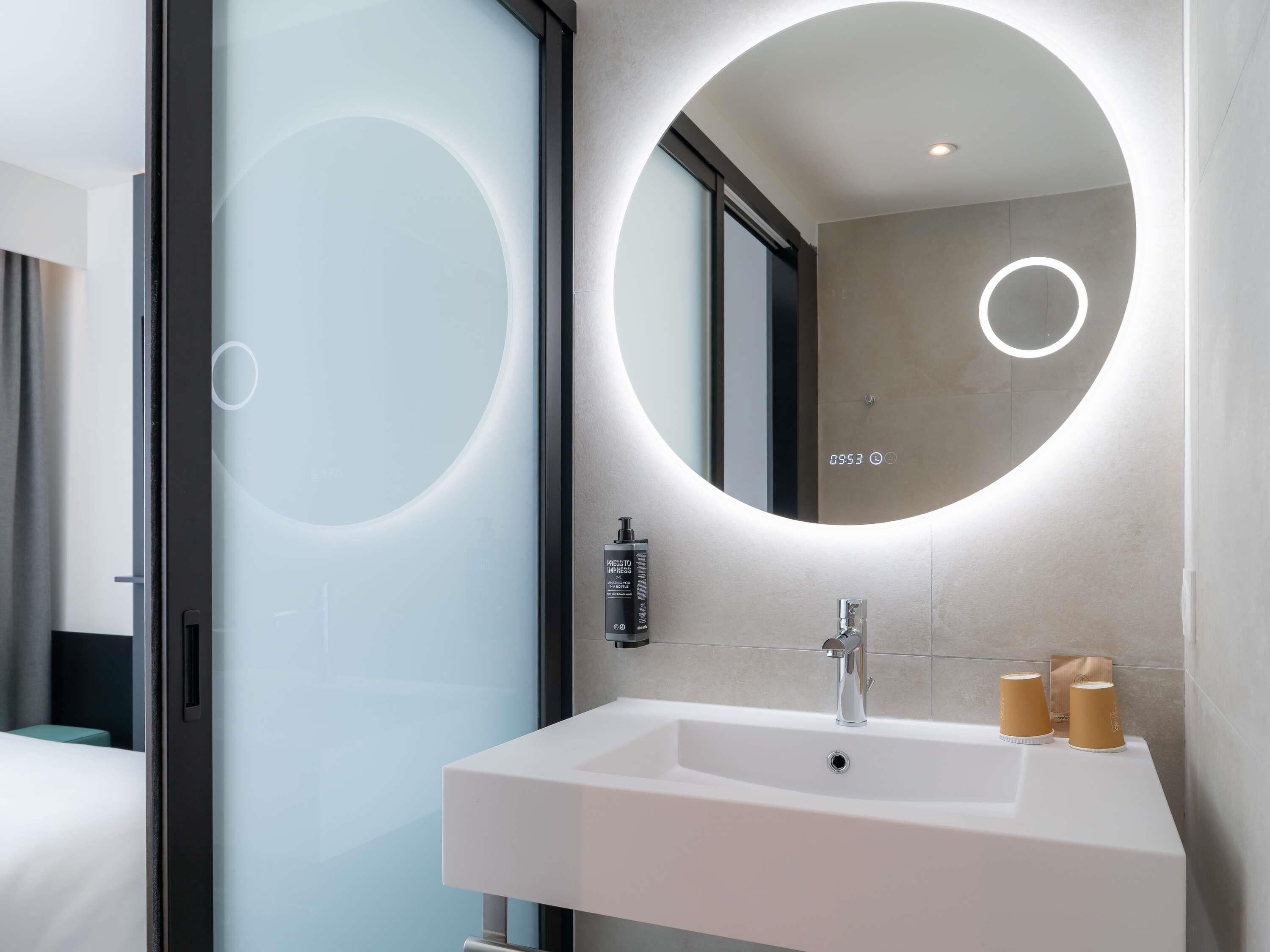 A modern bathroom with a large mirror, a white sink, and a shower area.