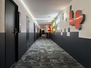 A hallway with doors, a patterned carpet, and a wall with a geometric design. - ibis Styles Béziers Centre (Béziers)