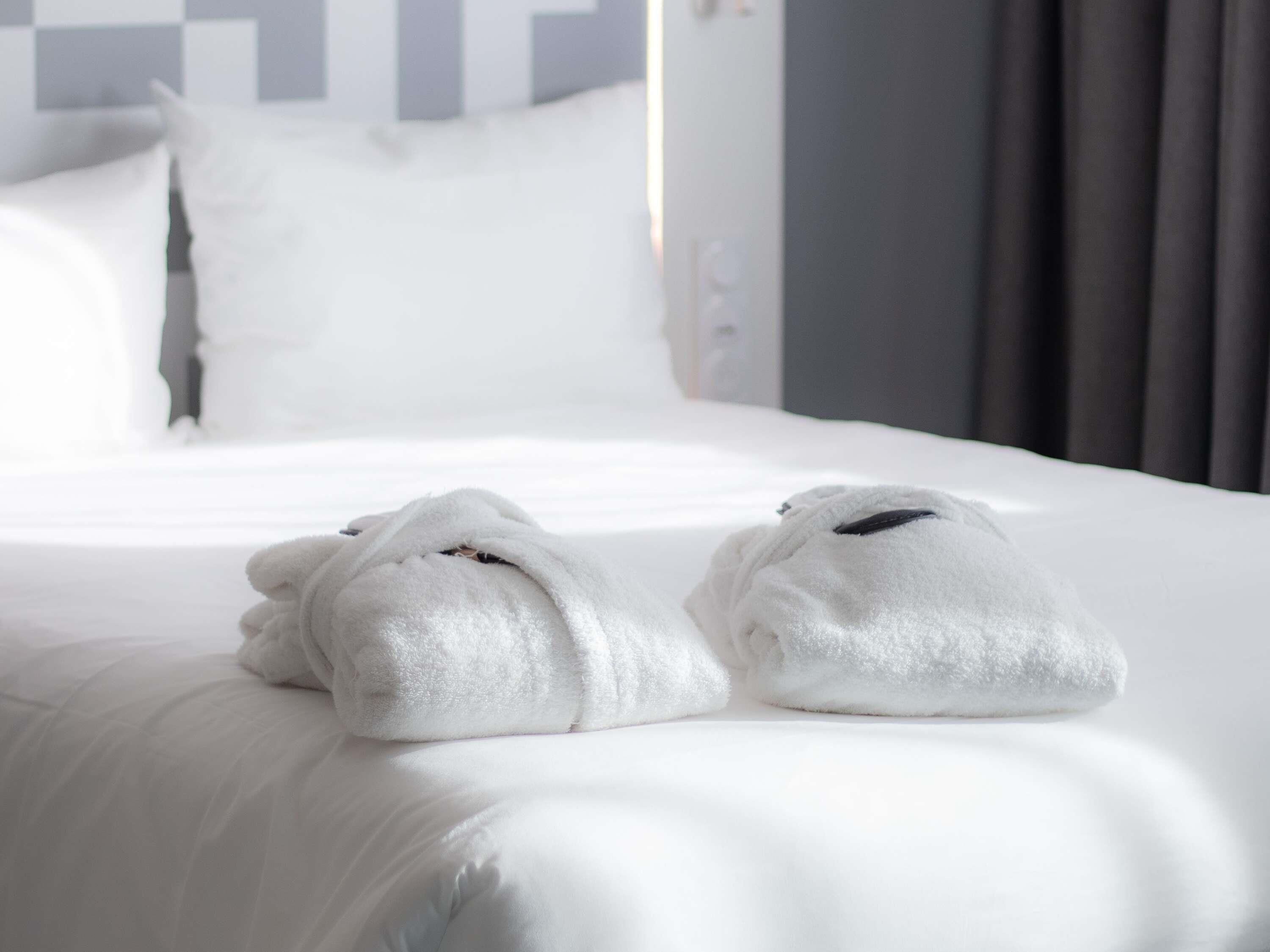 Ein ordentlich bezogenes Bett mit weißen Leinentüchern und zwei gefalteten Handtüchern.