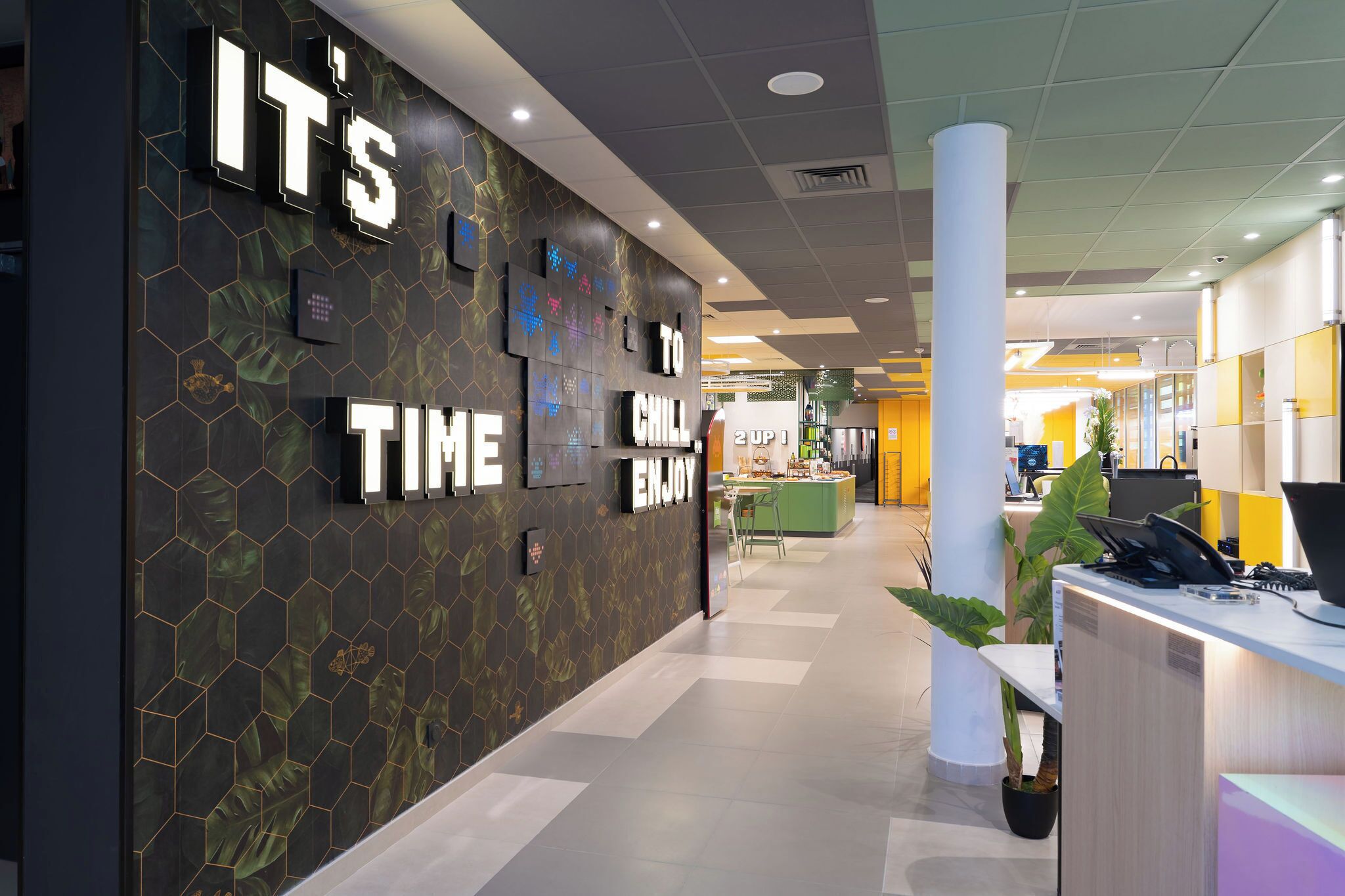Un interior moderno con una pared de diseño hexagonal, una mesa de recepción y un mostrador con un letrero que dice 'IT'S TIME TO CHILL ENJOY'.