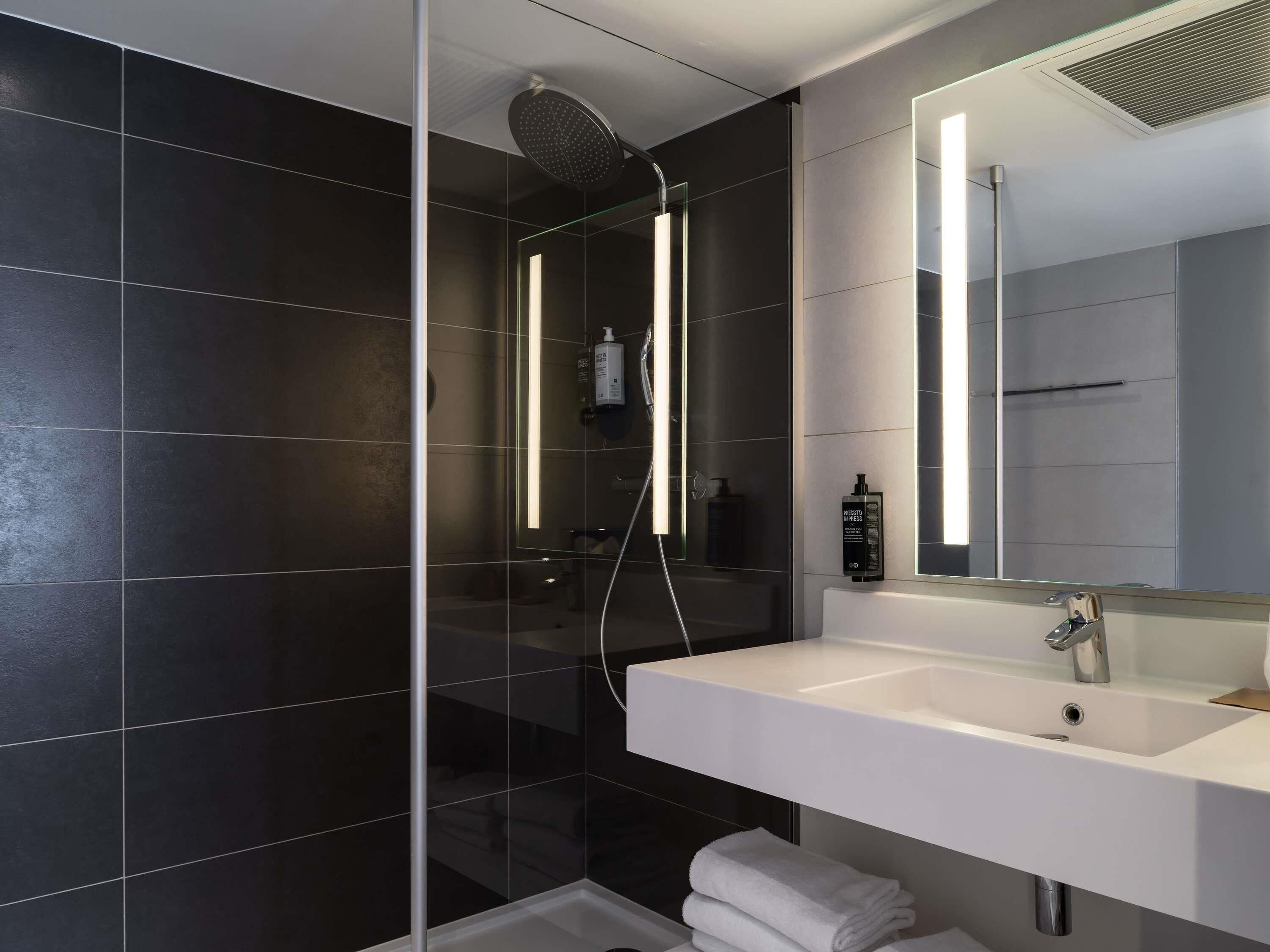 Un baño moderno con ducha de vidrio, un lavamanos blanco y un espejo grande.
