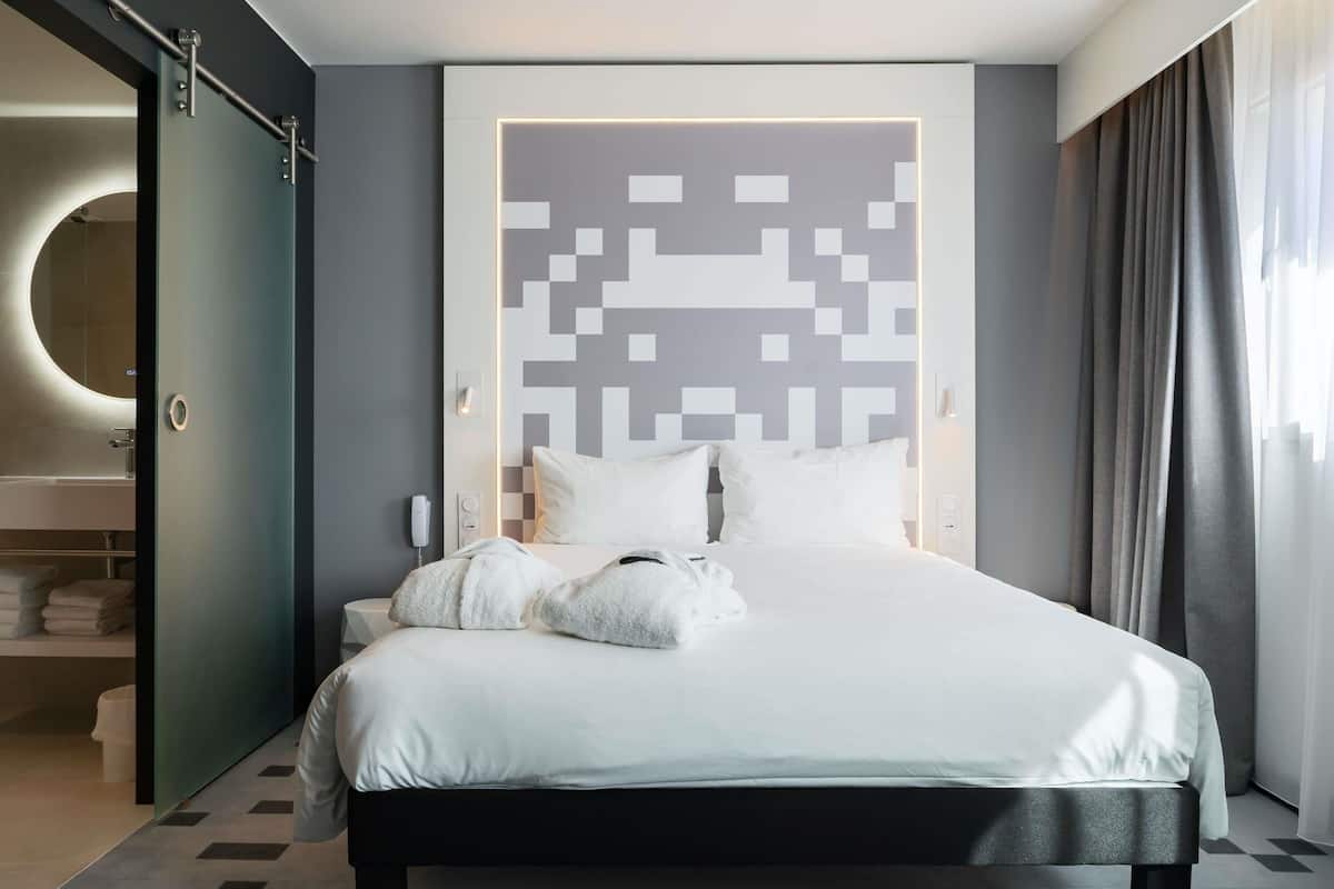 Ein modernes Hotelzimmer mit Bett, einem Badezimmer mit rundem Spiegel und Blick auf die Stadt.