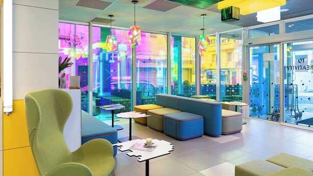 A modern interior with seating areas, tables, and a glass wall offering a view of the street. - ibis Styles Béziers Centre (Béziers)