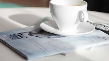 Une tasse de café blanche sur une table blanche, avec un magazine dont la couverture est bleue.