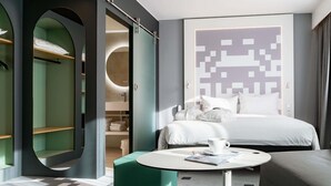 A modern hotel room with a bed, a round coffee table, a green ottoman, and a wardrobe with a circular mirror. - ibis Styles Béziers Centre (Béziers)