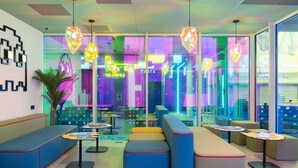 A modern lounge area with colorful seating, pendant lighting, and a view into a vibrant interior space. - ibis Styles Béziers Centre (Béziers)