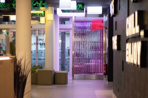 A modern hotel lobby with a glass door entrance, a fire extinguisher, and a seating area with ottomans.