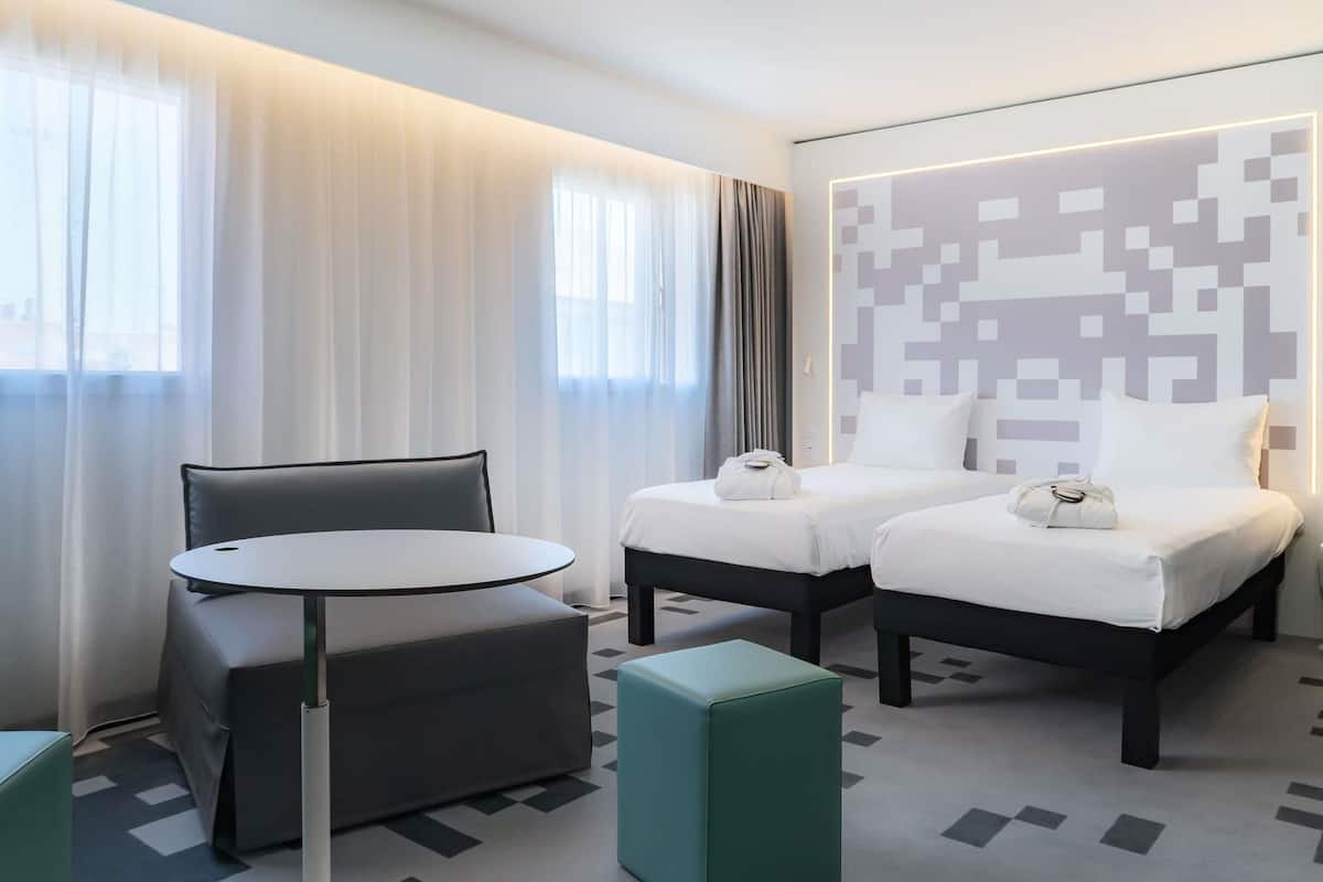 Ein Hotelzimmer mit zwei Betten, einem kleinen runden Tisch und einem grünen Hocker.