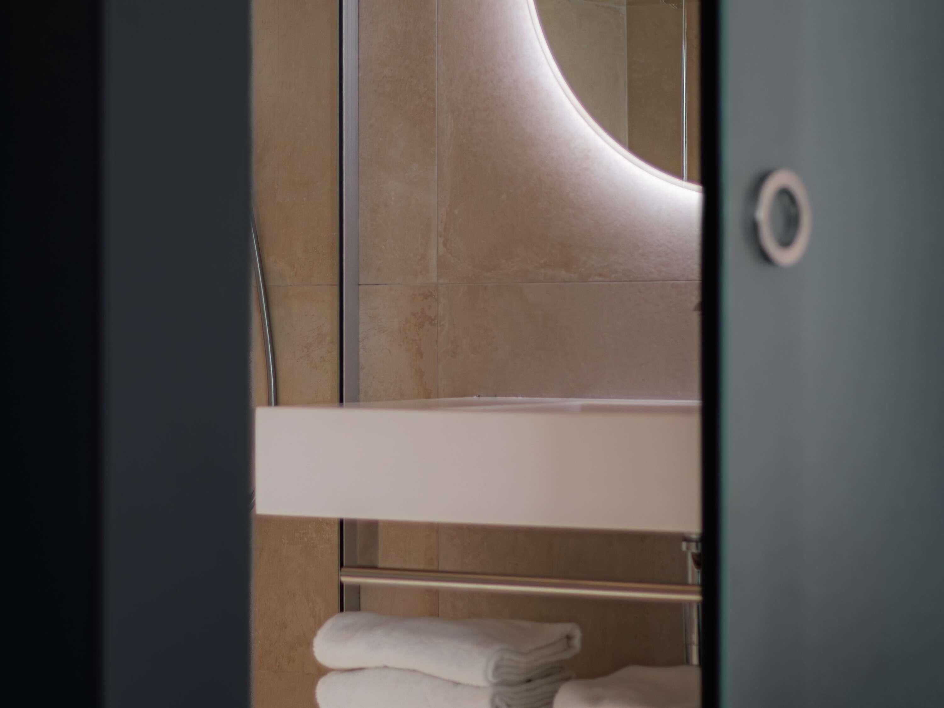 Ein Badezimmer mit weißem Waschbecken, einem Handtuchhalter mit gefalteten Handtüchern und einem Spiegel mit gebogener Rahmung.