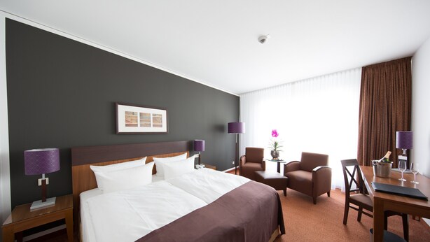 A hotel room with a large bed, two armchairs, a small table, and a desk with a chair.