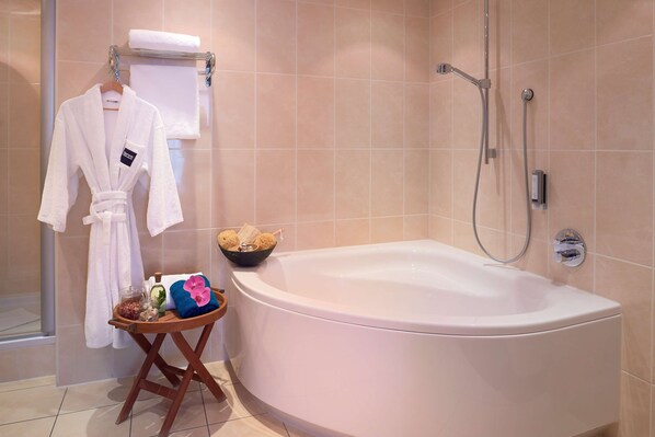 Une salle de bain avec une grande baignoire, un porte-serviettes avec un peignoir blanc et une petite table sur laquelle sont posés des articles de toilette.