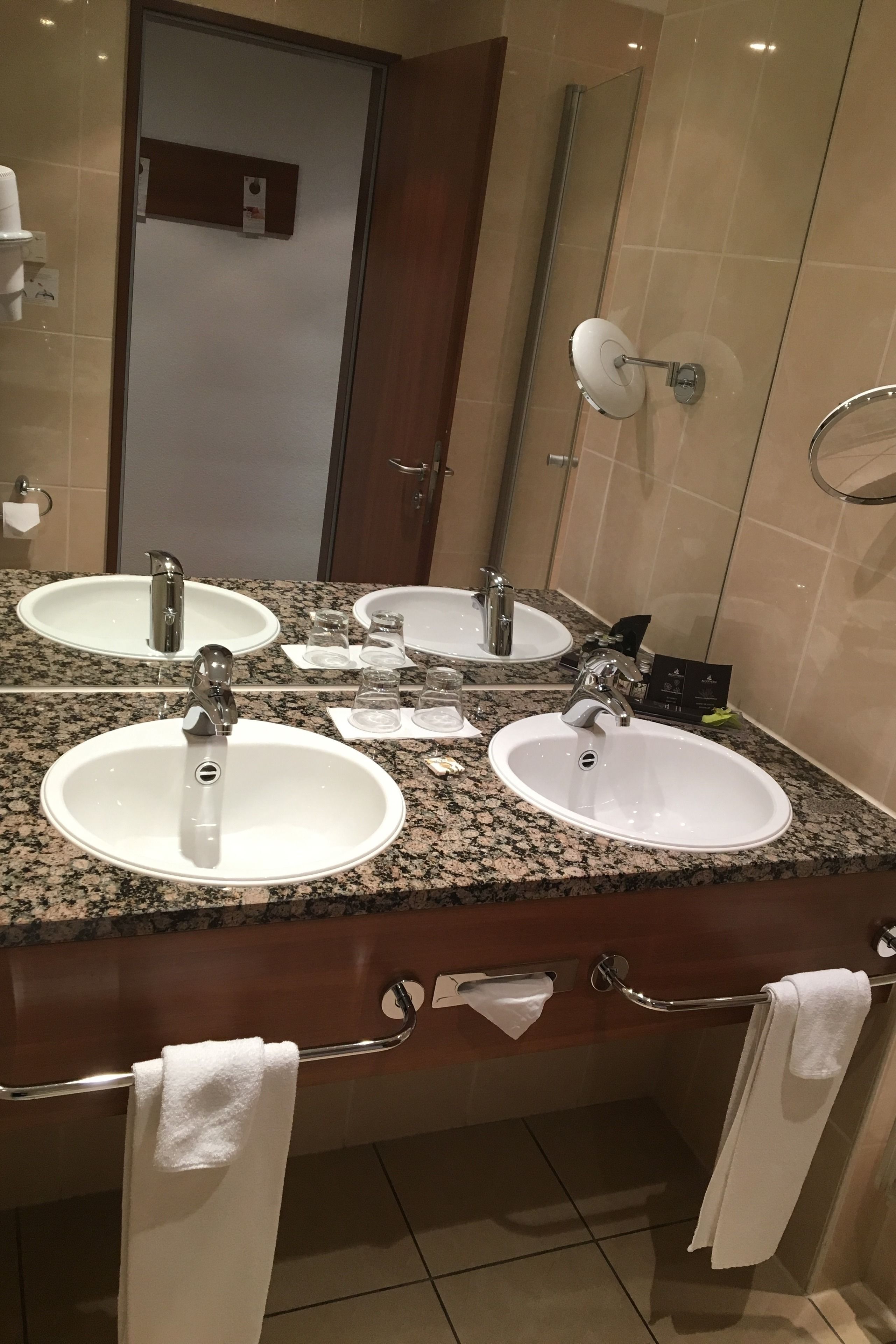 Un baño con tres lavamanos, un espejo grande y un perchero para toallas.