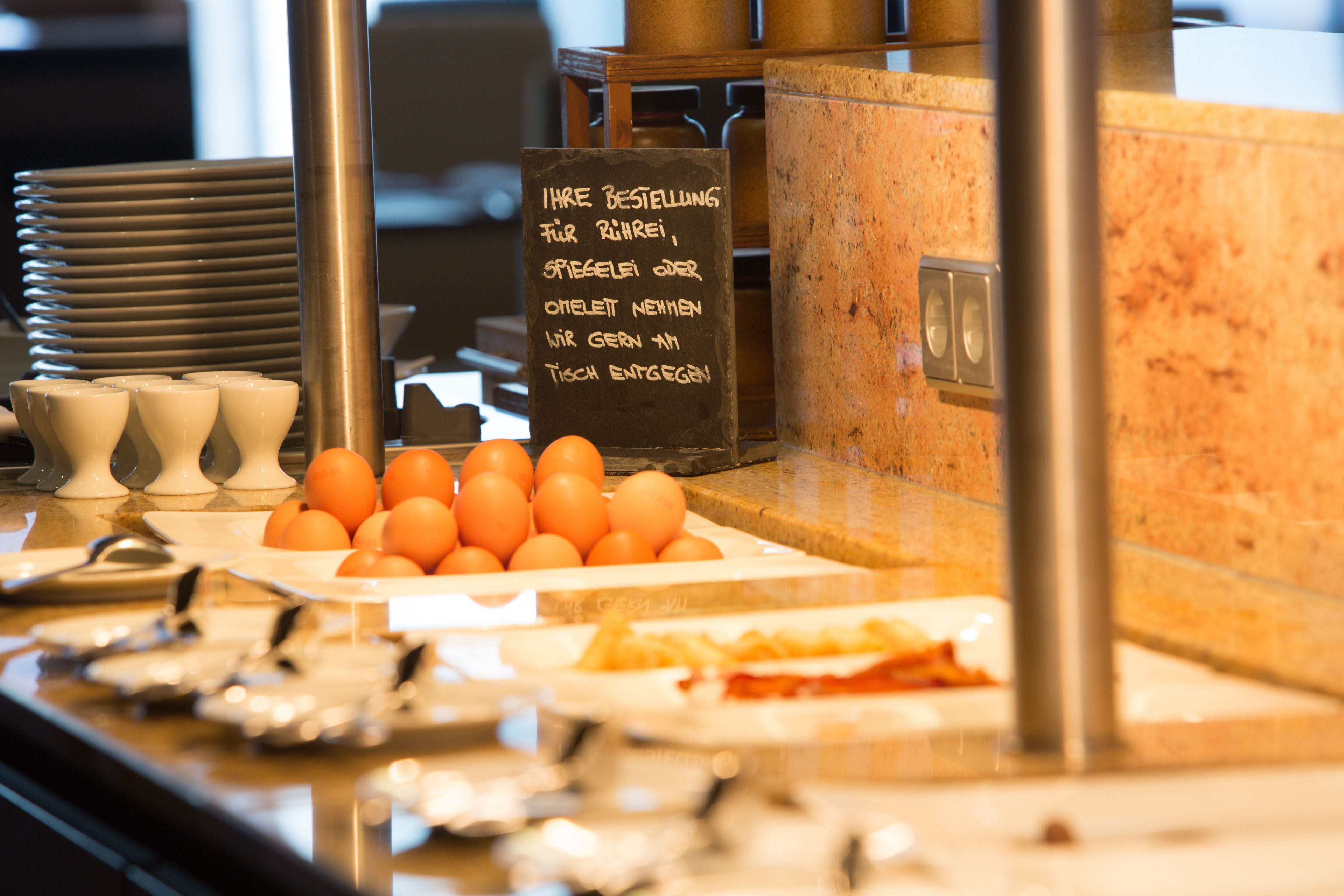 Un buffet avec des assiettes remplies d’œufs, une pancarte en allemand et une pile d’assiettes.