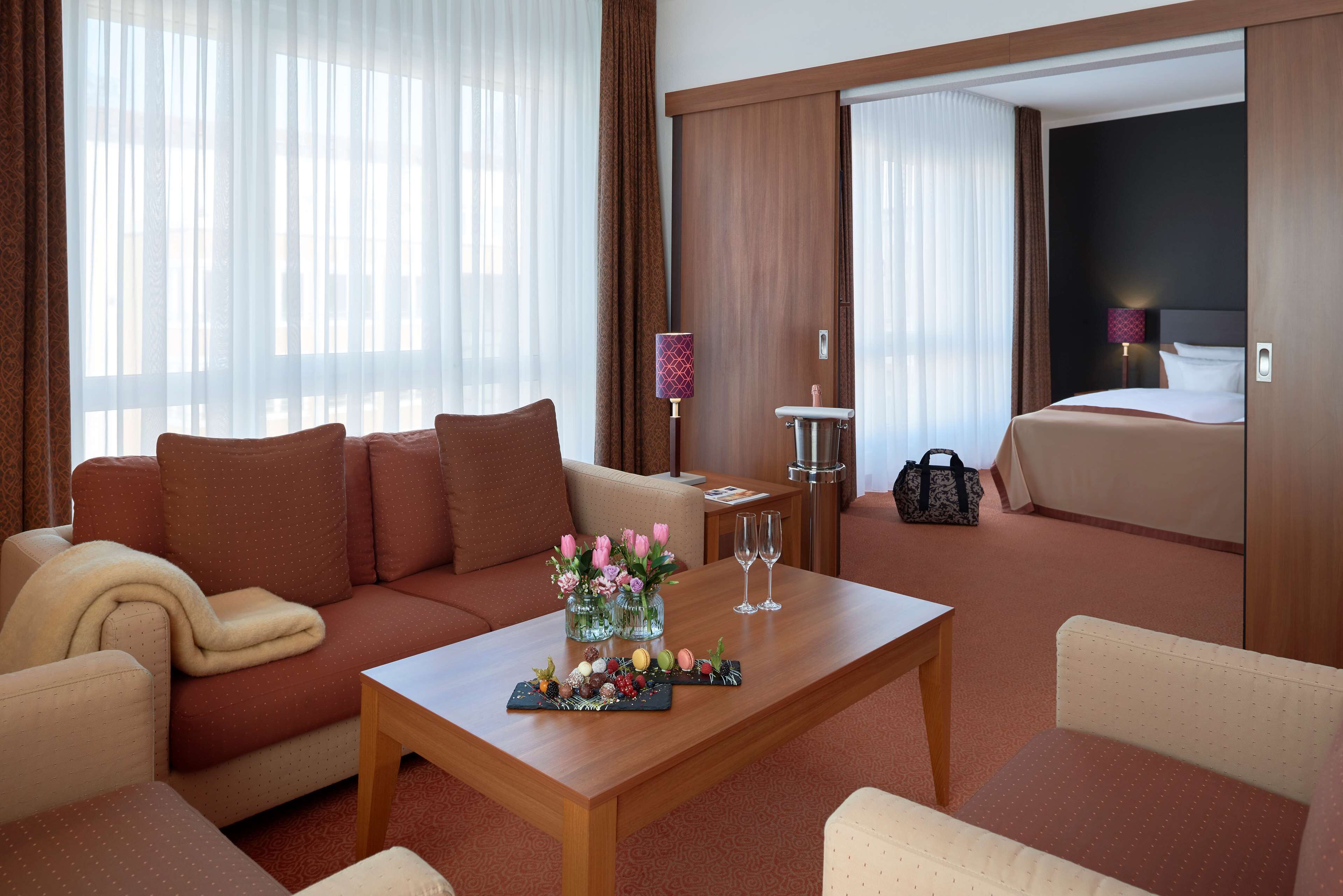 Une chambre d’hôtel avec un canapé, une table basse agrémentée d’un arrangement floral, une table de chevet avec une lampe et un lit.