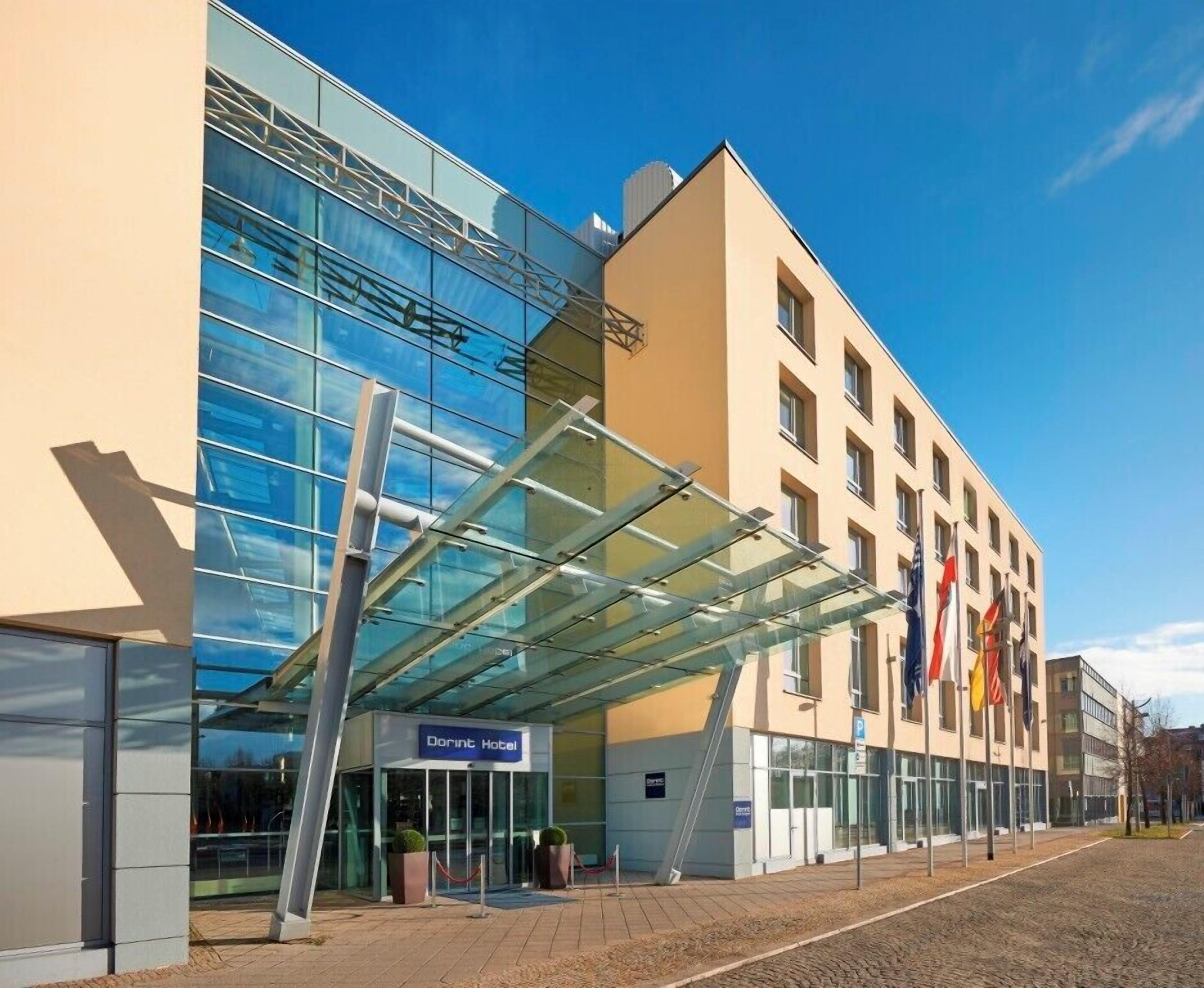 A Dorint Hotel with a modern glass facade, a covered entrance, and multiple flags.