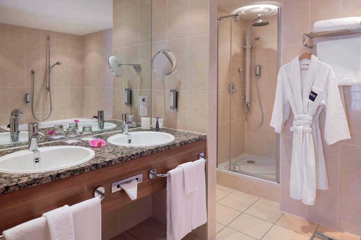 Un baño moderno con dos lavamanos, un espejo grande, una zona de ducha y una bata colgada en la pared.