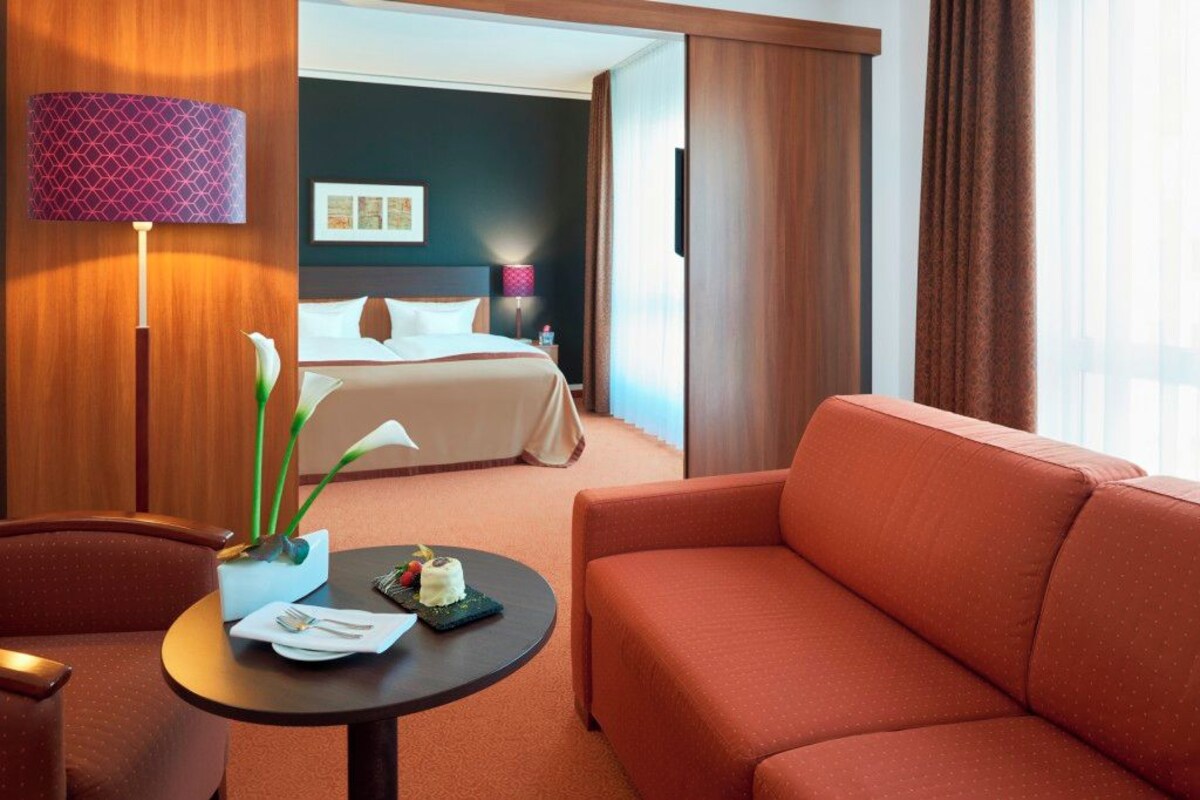 A hotel room with a bed, a sofa, a table with a plate of food, a lamp, and a plant.
