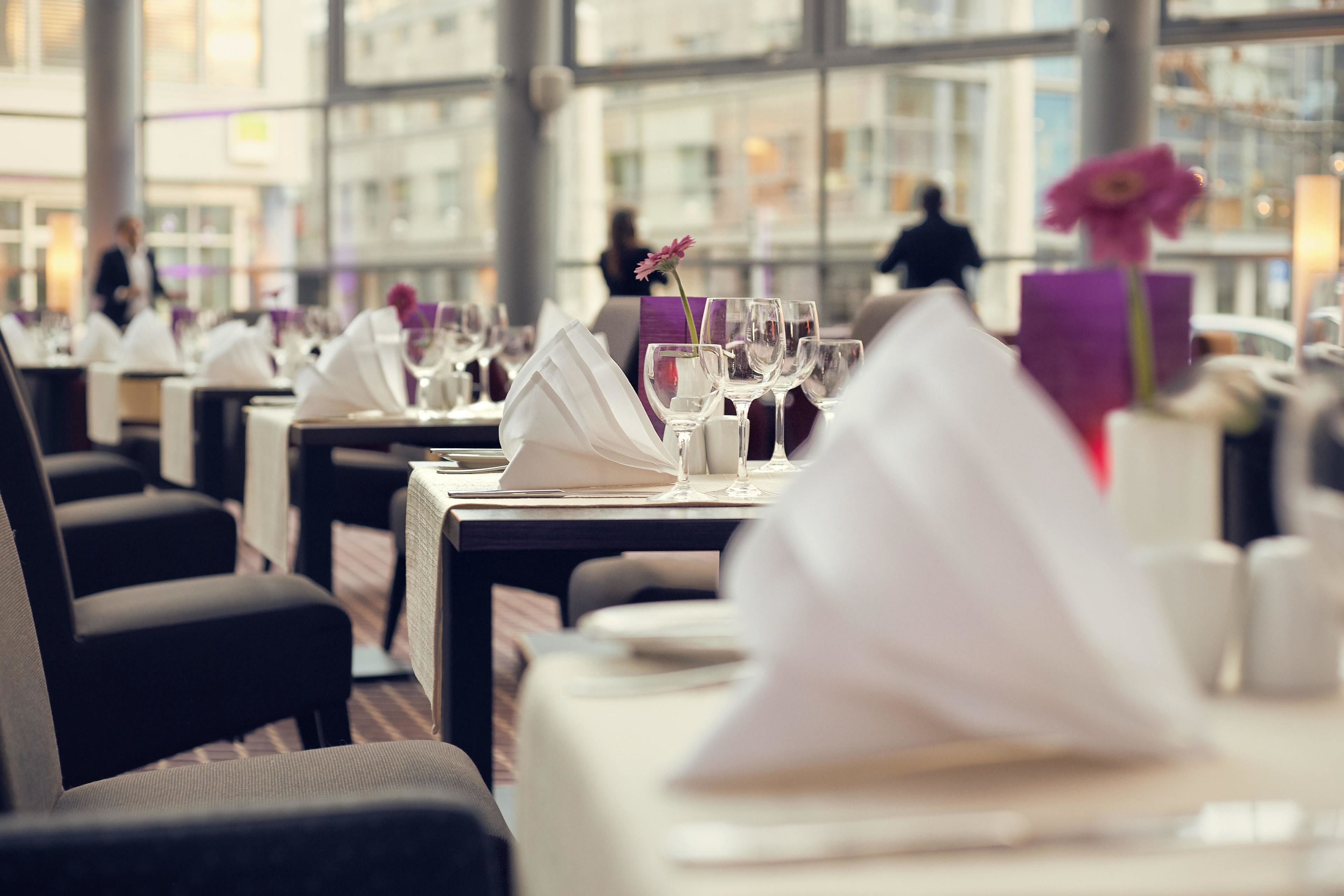 En restaurant med borde dækket til spisning, hvide duge og servietter.