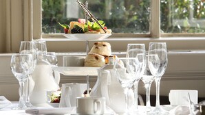 A table set with clear glassware, a teapot, and a tiered dessert plate with pastries and fruit. - Pendley Manor (Tring)