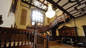 A grand staircase with ornate woodwork, a large chandelier, and a fireplace in a spacious hall with patterned flooring. - Pendley Manor (Tring)