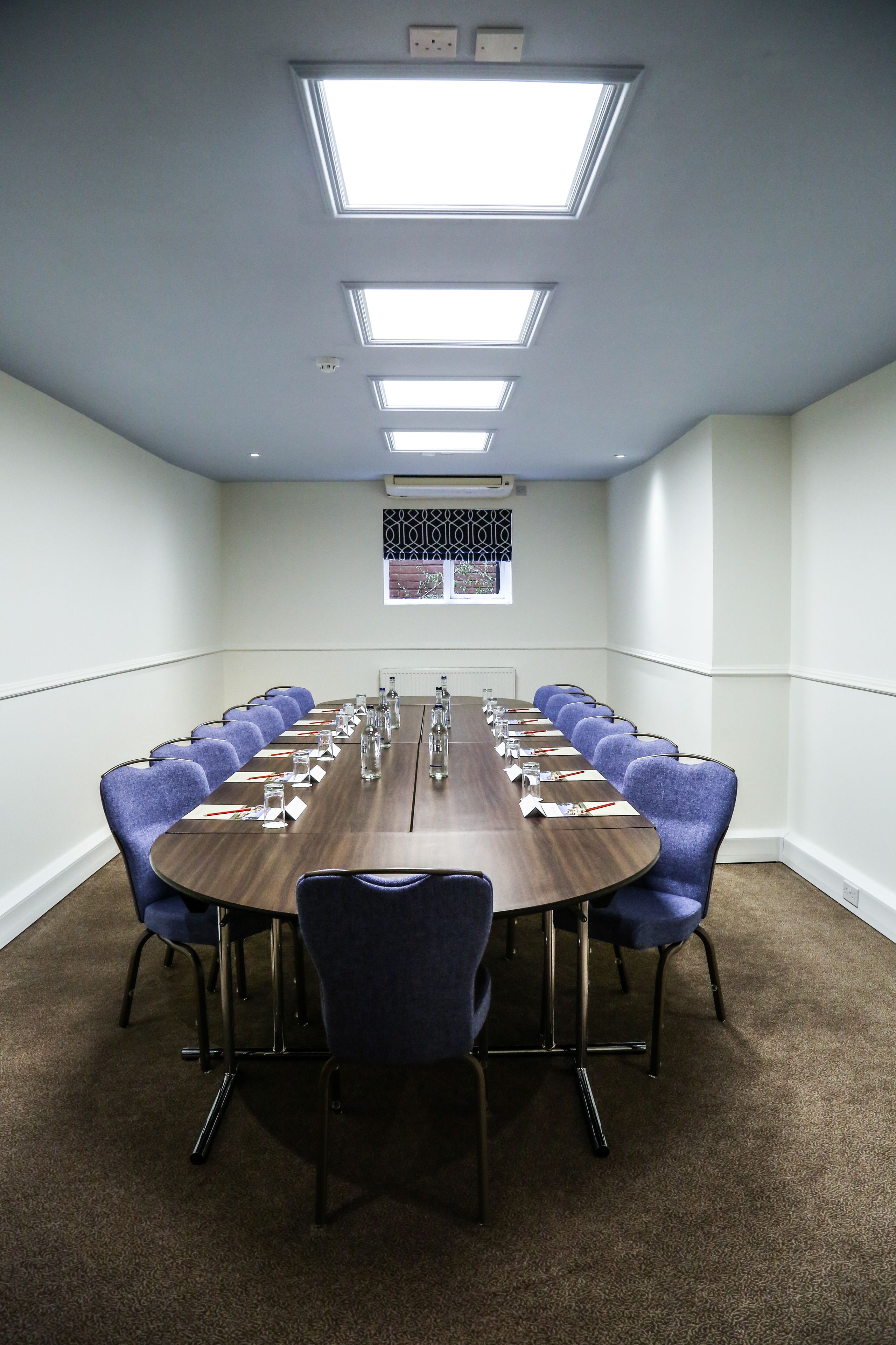 A conference room with a long table, blue chairs, and overhead lighting.