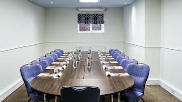 A conference room with a long table, blue chairs, and overhead lighting.