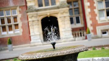 A stone fountain with water spouting from its center, set against a building with a brick facade and arched entrance.