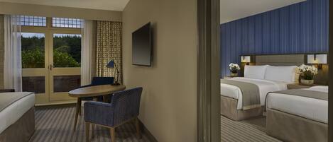 Habitación de hotel con cama, escritorio con silla, televisor y vista a zonas verdes por la ventana.