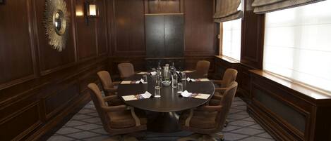 Un salón de conferencias con una mesa redonda, ocho sillas, una araña y un espejo grande en la pared.