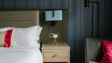 A neatly made bed with white and red pillows, a bedside table with a vase of flowers, and a wall-mounted light fixture.