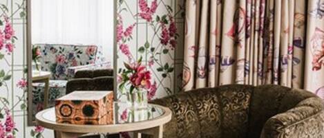 A room with floral wallpaper, a patterned sofa, a round wooden table, and a mirror.