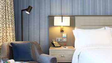 A hotel room with a bed, a nightstand with a lamp, a telephone, and a wall-mounted light.
