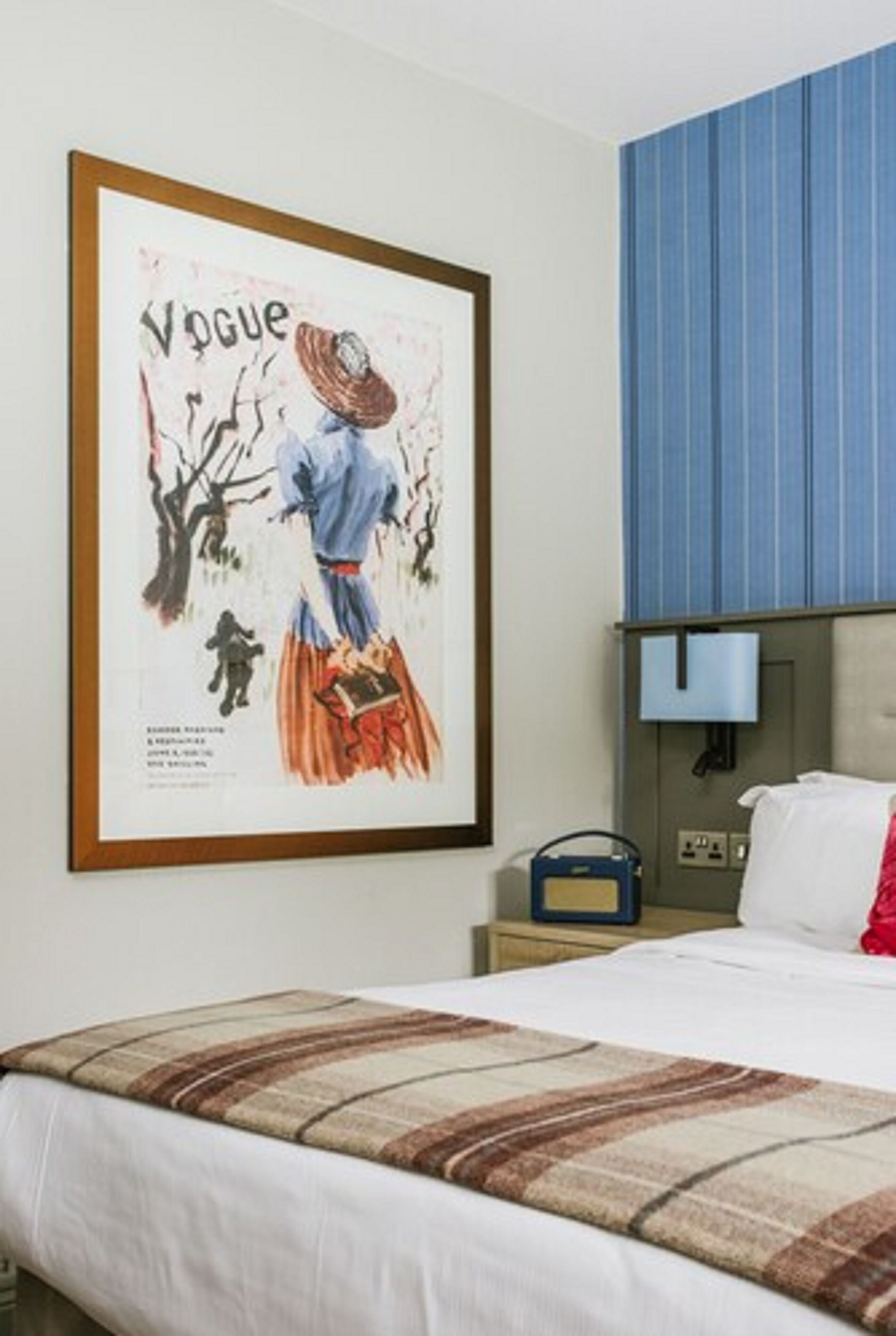 A hotel room with a bed, a framed picture on the wall, a blue-striped wall, and a bedside table with a lamp.