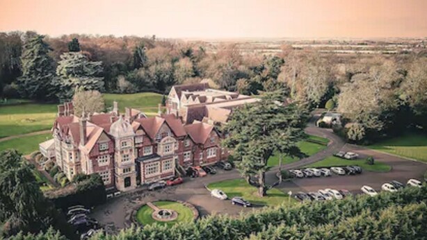 A large, historic building with a prominent tower, surrounded by lush greenery and a parking area. - Pendley Manor (Tring)