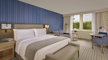 Une chambre d’hôtel avec un grand lit, des tables de chevet, une petite table avec une lampe, une chaise et une vue sur l’extérieur.