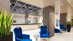 Un hall d’entrée moderne avec des fauteuils bleus, une table ronde et de grandes plantes en pot.