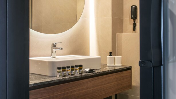 A modern bathroom with a large mirror, a sink, and a toilet. There are towels and toiletries on the counter. - Hersonissos Palace - All Inclusive (Hersonissos)